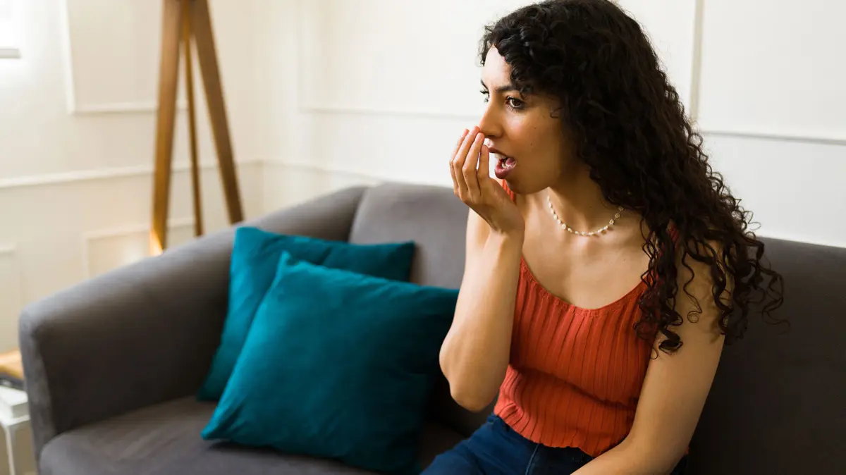 junge Frau sitzt auf dem Sofa und atmet in ihre Hand