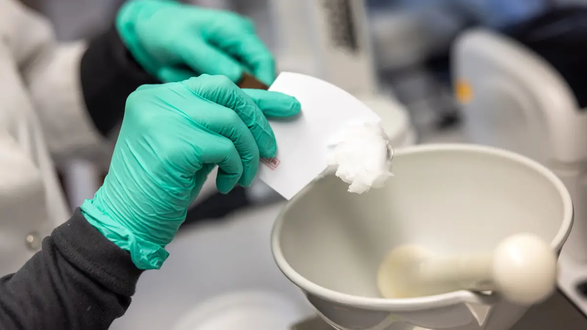 PTA mit einmalhandschuhen kratzt mit einem Kartenblatt weißes Vaselin von einem Pistill; davor steht eine Fantaschale mit Pistill
