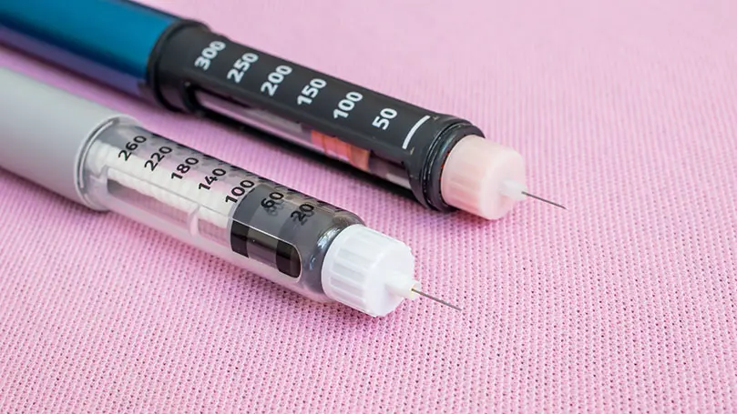 Zwei Insulinpens liegen auf rosafarbenem Stoff