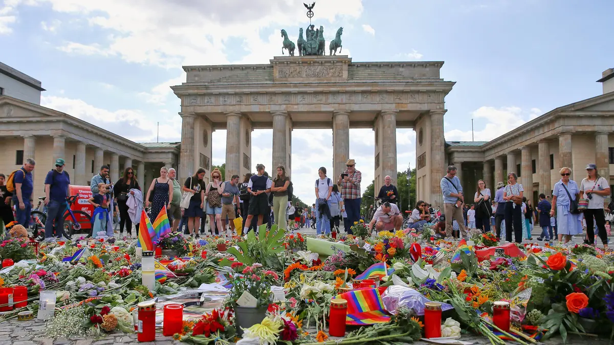 Menschen stehen vor dem Brandenburger Tor, auf dem Boden liegen Blumen und Kerzen in Gedenken an die Opfer des CSD