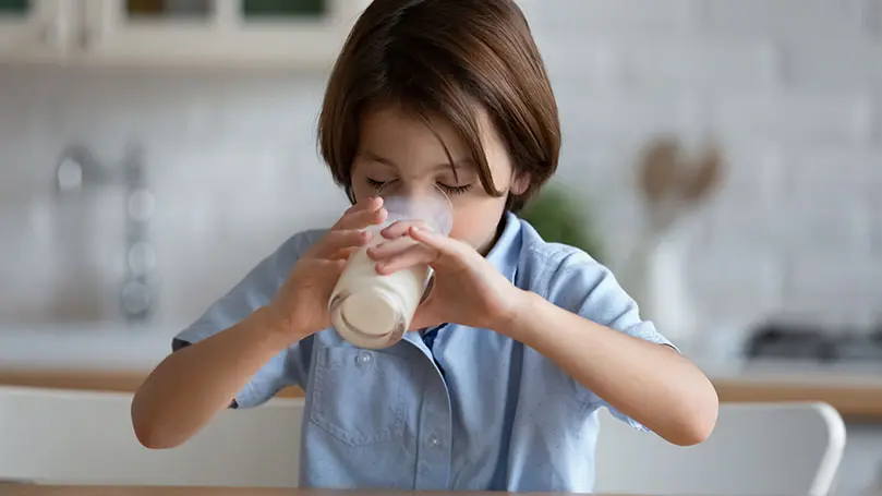 dunkelhaariger Junge trinkt in der Küche stehend ein Glas Milch