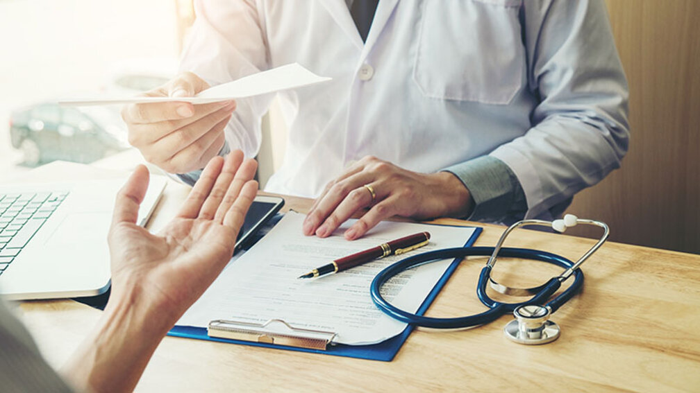 Arzt reicht Patienten ein Rezept