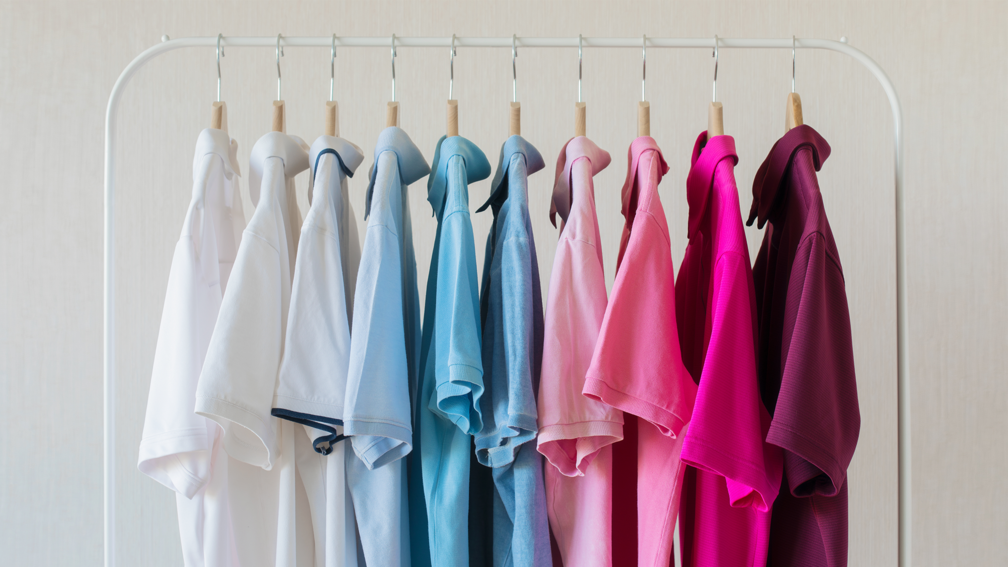 Auf einer weißen Kleiderstange hängen 10 Poloshirts farblich sortiert von weiß über blau bis rot