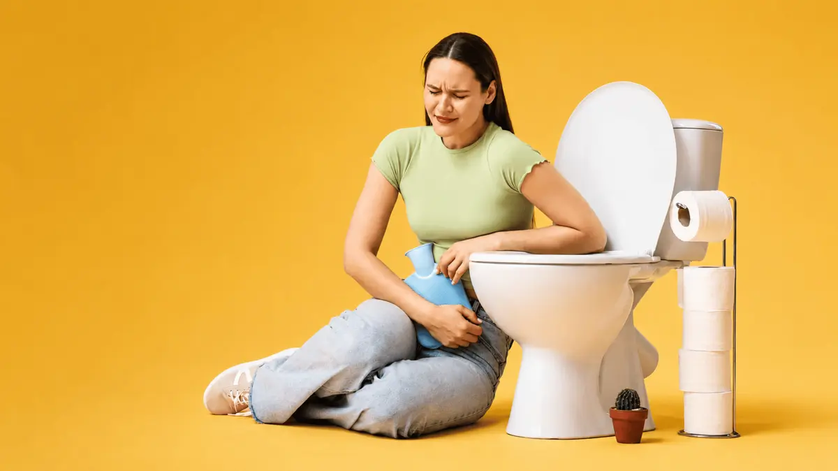 Frau die Schmerzen im Unterleib hat und neben der Toilette sitzt