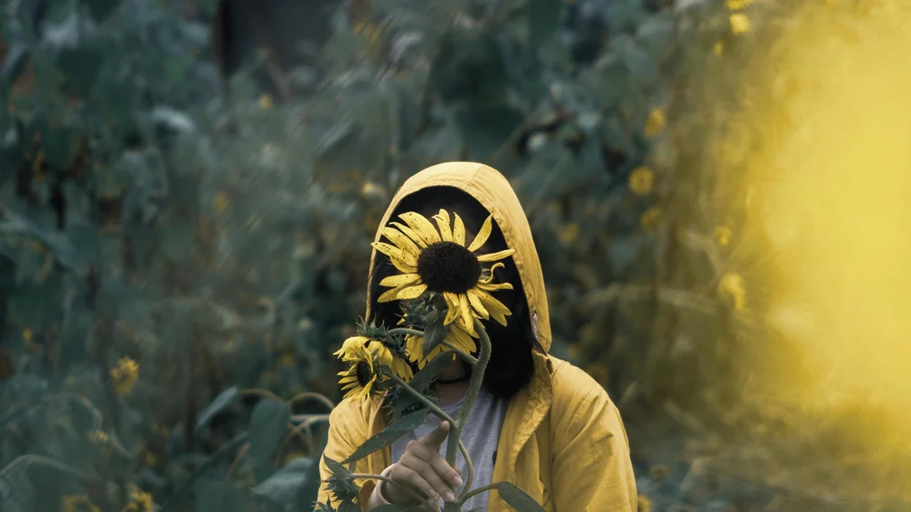PErson hält sich Sonnenblumen vor das Gesicht