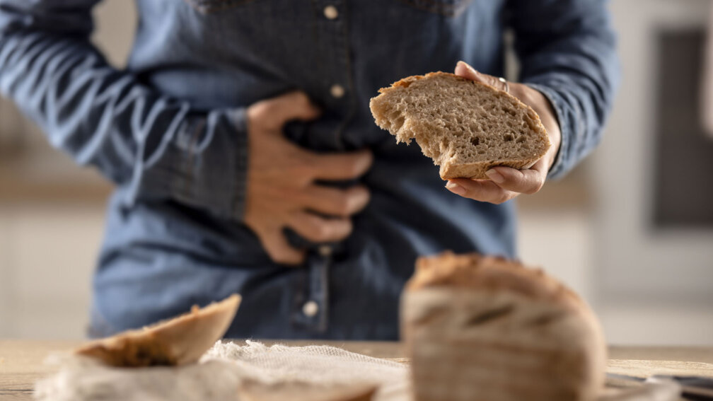 Frau hält Scheibe Brot in der Hand und fasst sich mit der anderen Hand an den Bauch