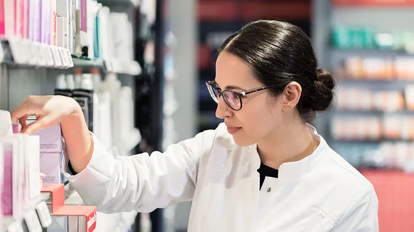 PTA in weißem Kittel steht vor Regal mit Kosmetik