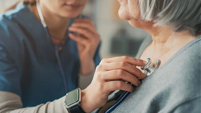 MFA hört das Herz einer Seniorin mit Stethoskop ab
