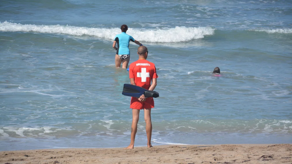 Rettungsschwimmer steht am Rand des Gewässers; zwei Leute befinden sich im Wasser