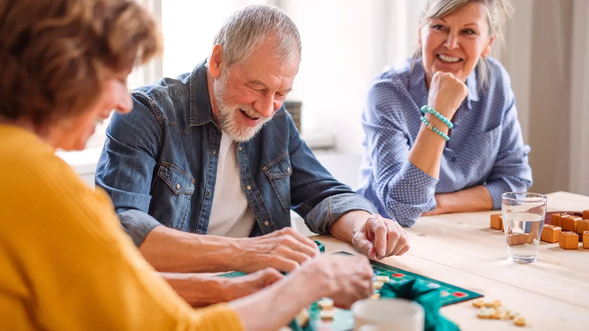 drei Senioren sitzen an einem Tisch und spielen ein Brettspiel