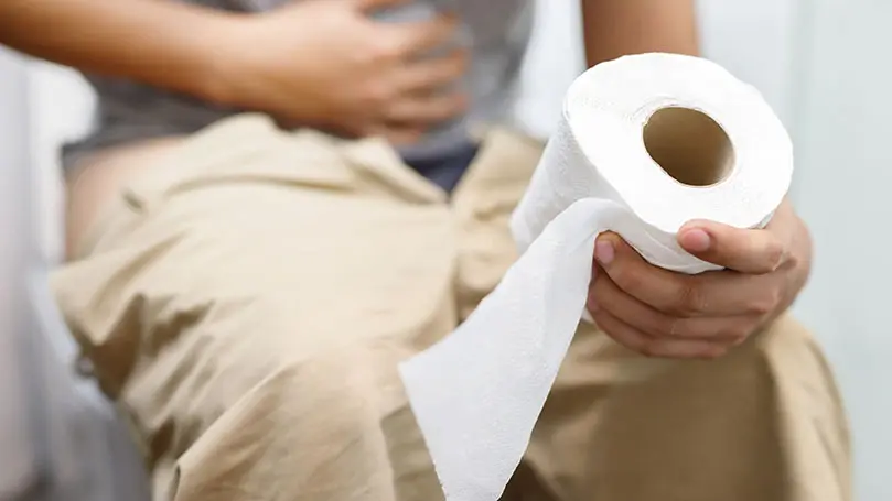 Mann mit Durchfall sitzt auf Toilette und hält Klopapierrolle in der Hand