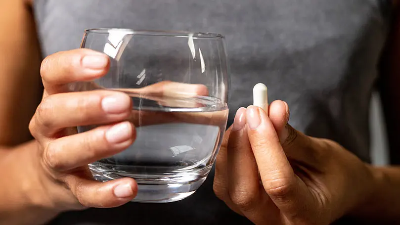 Fokus auf weibliche HÄnde, die ein gefülltes Wasserglas und eine Kapsel halten
