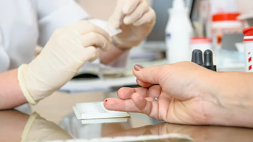 Im Fokus ein Ringfinger mit blutender Einstichstelle