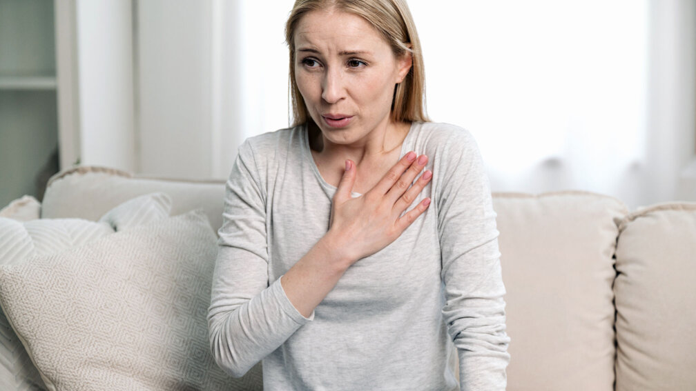Frau atmet und fasst sich mit der Hand an die Brust
