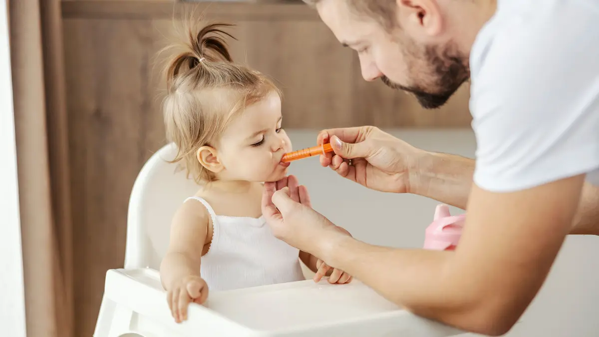 Kleinkind sitzt im Hochstuhl, Vater verabreicht dem Mädchen mittels einer Dosierspritze ein Medikament