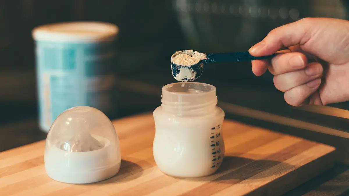 Säuglingspulver wird mit einem Dosierlöffel in eine Milchflasche gegeben