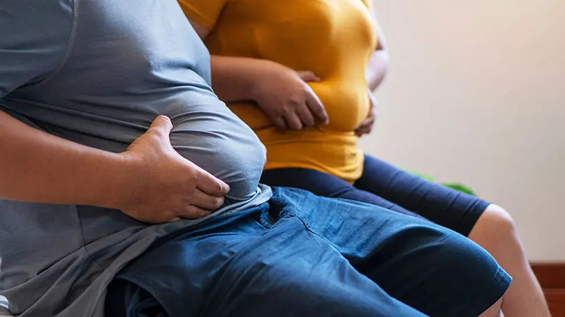 Mann und Frau halten ihren Bauchspeck fest, während sie auf einem Sofa sitzen