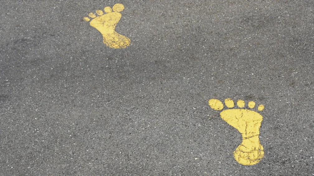 Zwei gelbe Fußabdrücke auf Asphalt