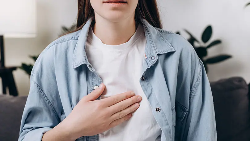 dunkelhaarige Frau in weißem Tshirt und offenem Jeanshemd hält rechte Hand auf Brustbein