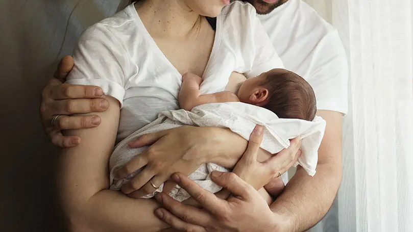 Vater hält Mutter im Arm, die ihr Baby stillt