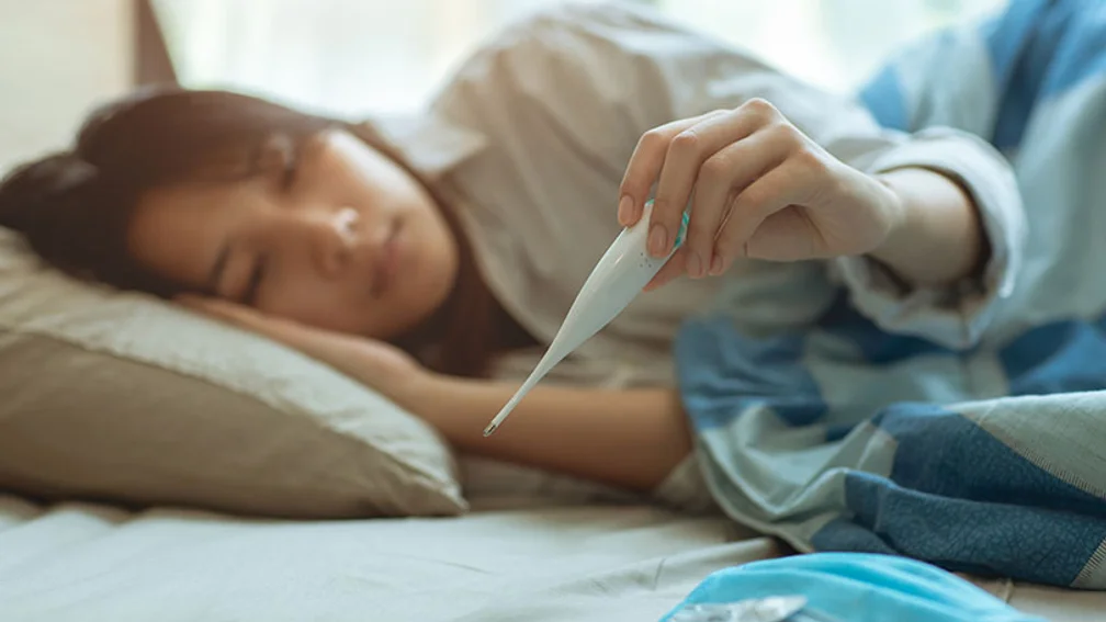 junge Asiatin liegt im Bett und schaut auf ein Fieberthermometer