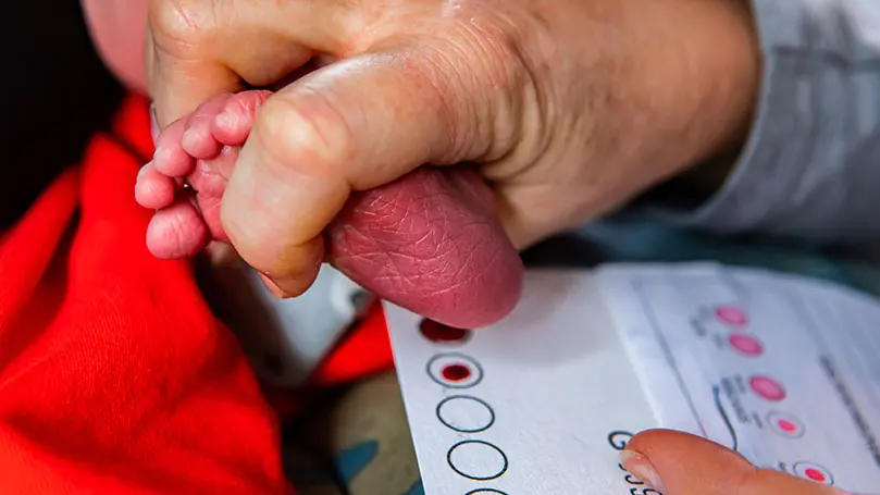 Babyfuß wird über eine Pappkarte mit Bluttropfen gehalten