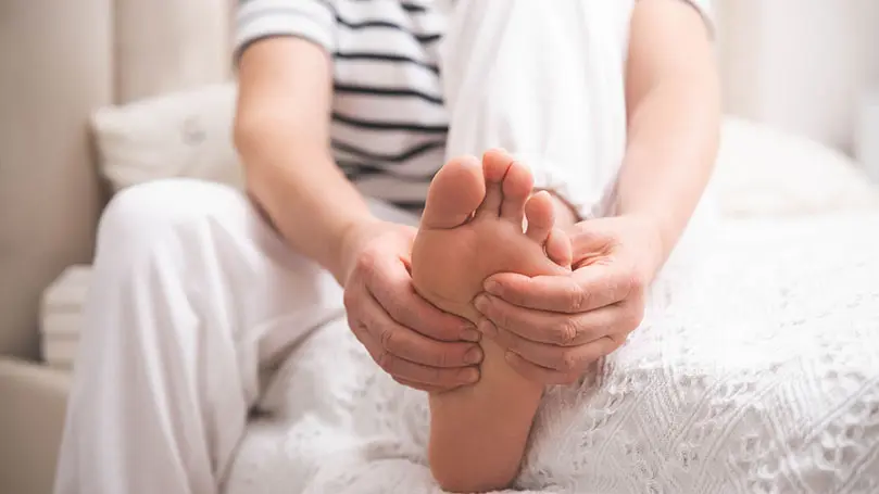 junge Frau sitzt auf einem Bett und hält linken Fuß in beiden Händen