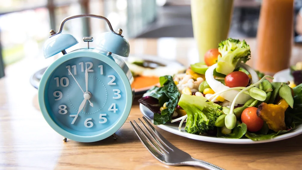 Teller mit verschiedenen, gesunden Lebensmitteln, daneben steht ein Wecker und eine Gabel liegt im Vordergrund