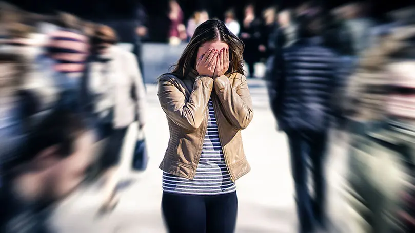 Ängstliche Frau steht mit Händen vor den Augen in einer Menschenmenge