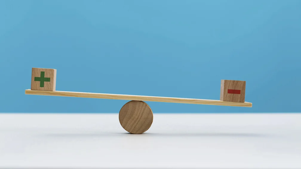 Holzwaage mit links einem Holzwürfel mit grünem Plus und rechts einem Holzwürfen mit rotem Minus