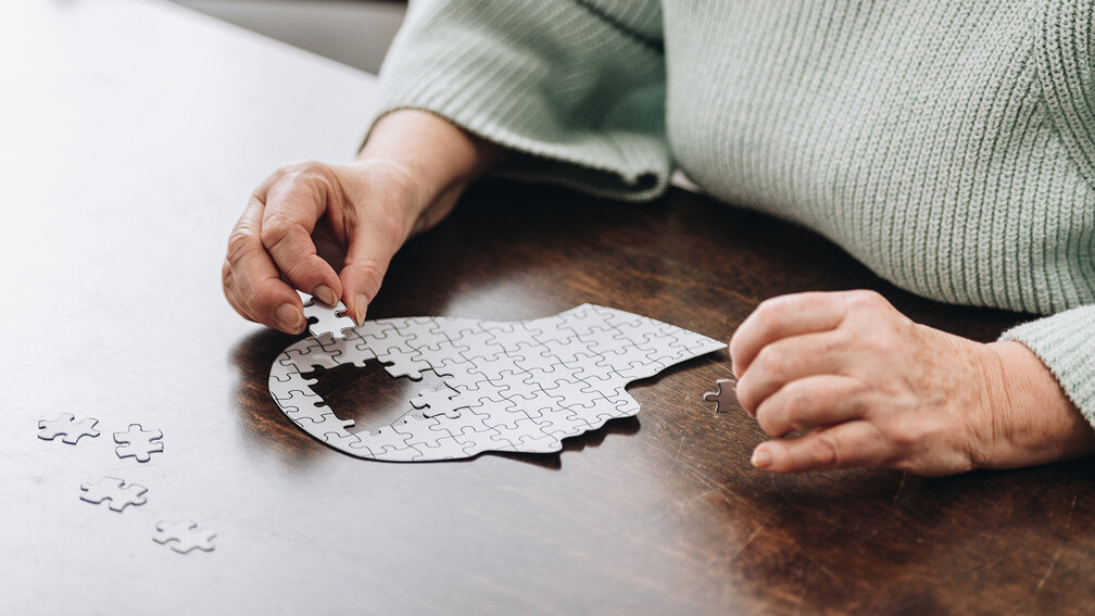 Seniorin setzt Puzzle in Form eines menschlichen Kopfes zusammen