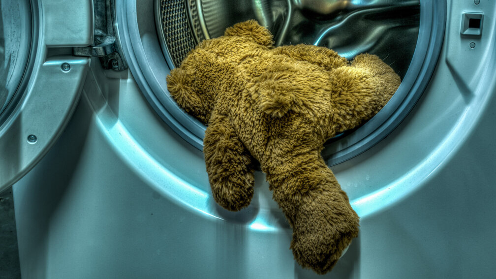 Teddybär hängt halb aus Waschmaschinentrommel