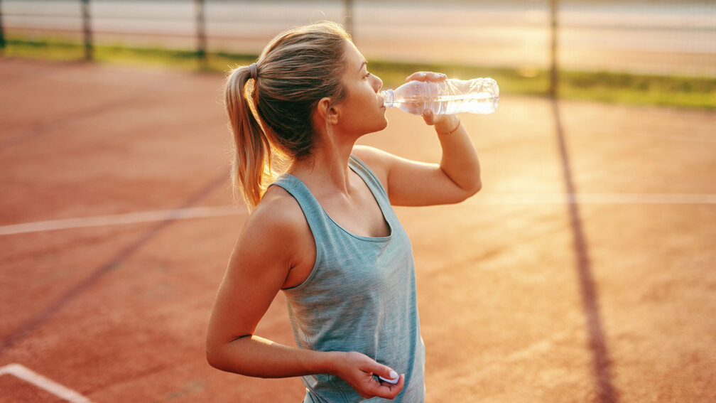 junge Frau trinkt beim Sport aus einer Flasche