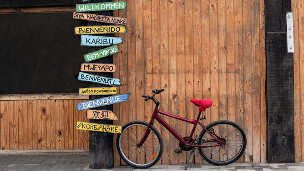 rotes Fahrrad neben mehrsprachigen Willkommensschildern