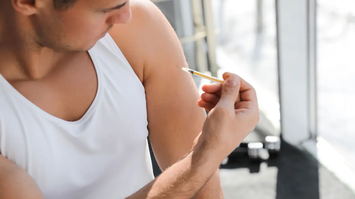 Mann spritzt sich Flüssigkeit mittels einer Injektionsspritze in den Oberarm