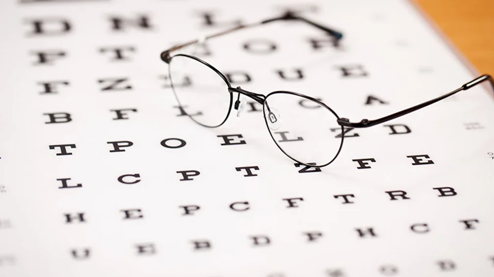 Brille mit schwarzem Gestell liegt auf Buchstabenblatt für Sehtests