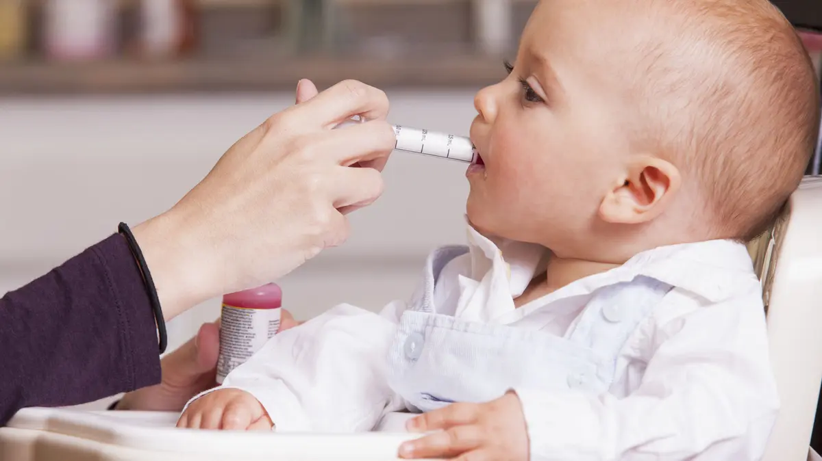 Mutter verabreicht Kleinkind Antibiotikasaft mit Dosierspritze