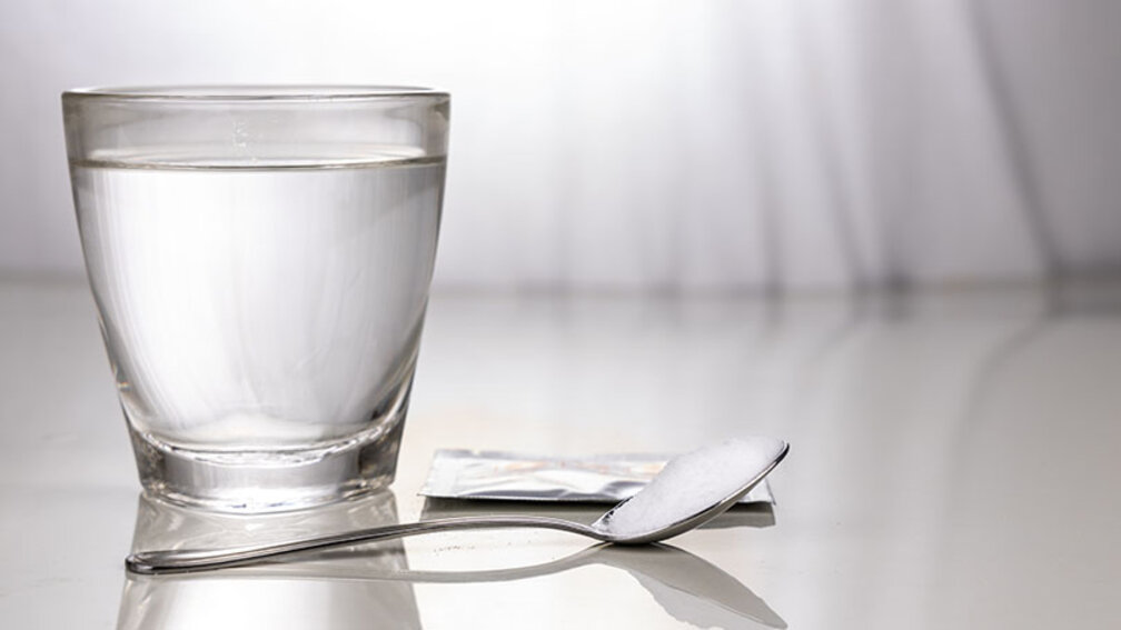 Mit Wasser gefülltes Glas hinter einem Löffel mit Pulver