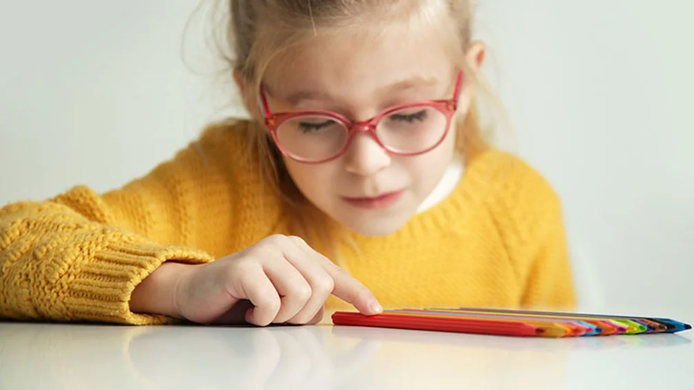 junges Schulmädchen mit roter Brille richtet Buntstifte exakt gleich aus