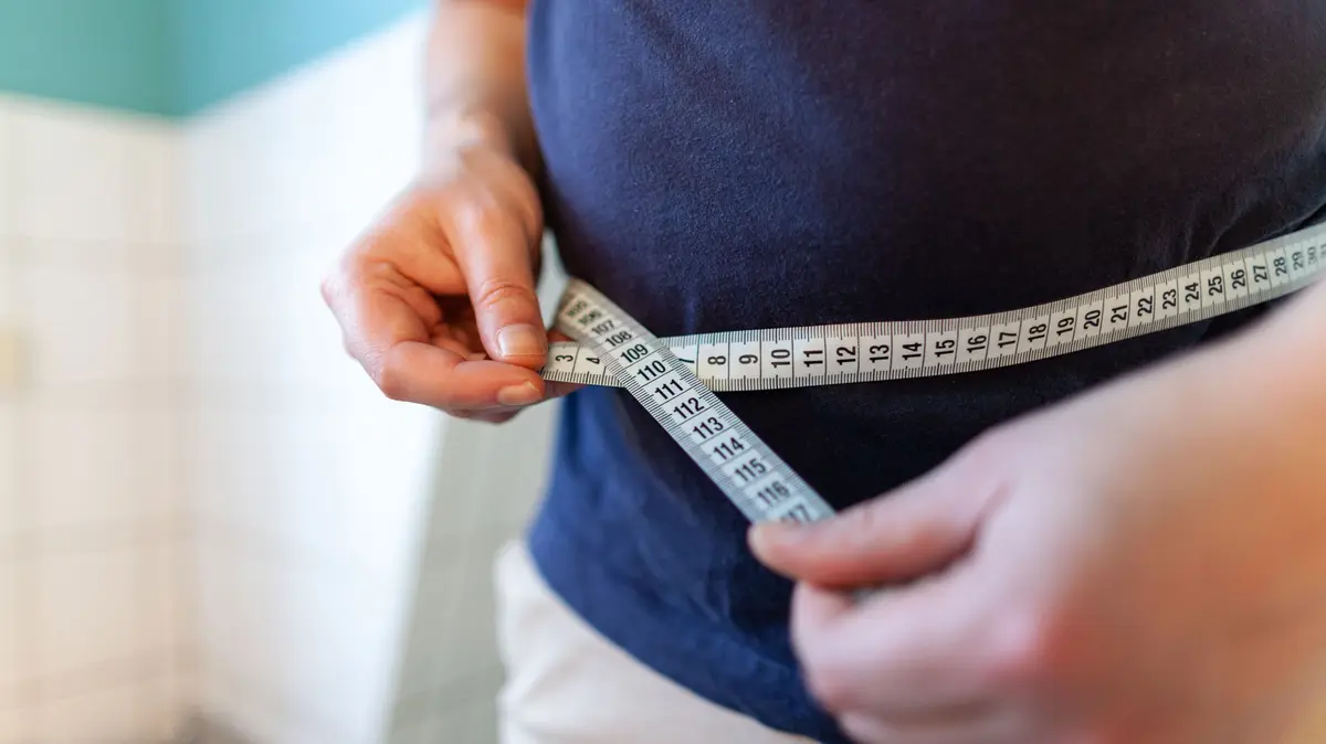 Mann hält sich Maßband um den Bauch