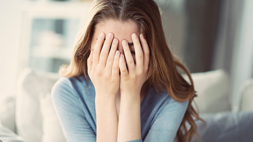 Junge Frau hält sich die Hände vors Gesicht