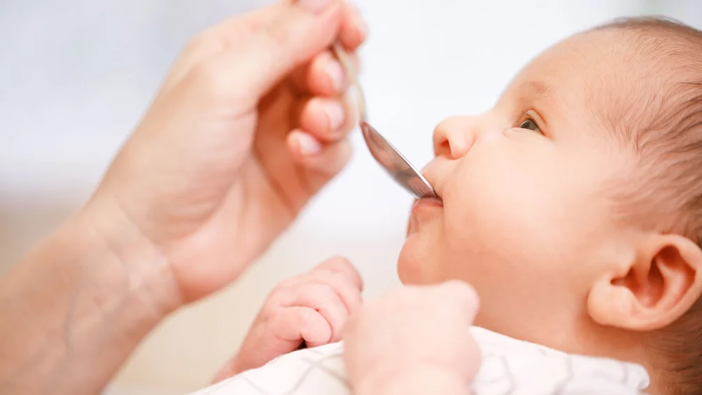 Mutter füttert Säugling mithilfe einem Löffel mit flüssigem Medikament 