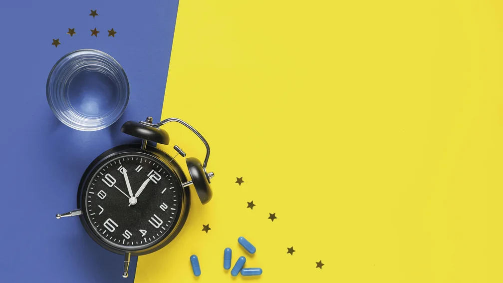 Bild von oben von einem Wasserglas, einem Wecker und Kapseln