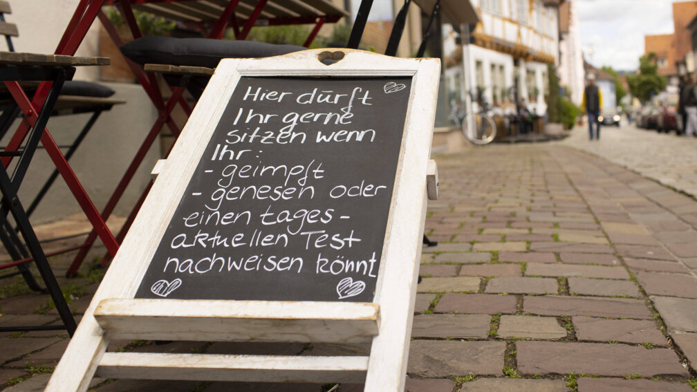 Umgeworfenes Tafelschild mit Text: Hier dürft ihr gerne sitzen wenn ihr geimpft, genesen oder einen tagesaktuellen Test nachweisen könnt