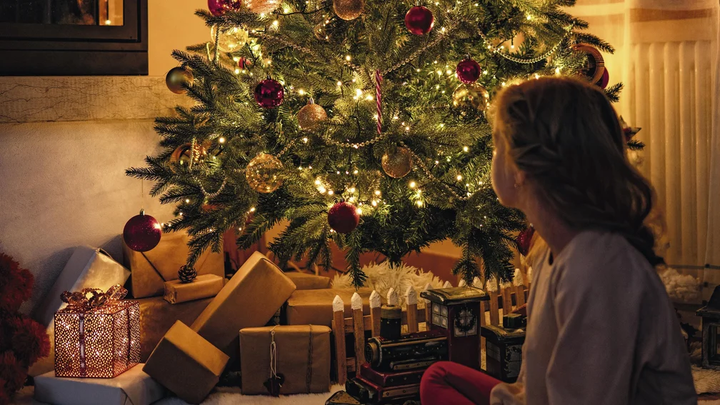 Mädchen sitzt vor einem geschmückten Weihnachtsbaum mit Geschenken darunter