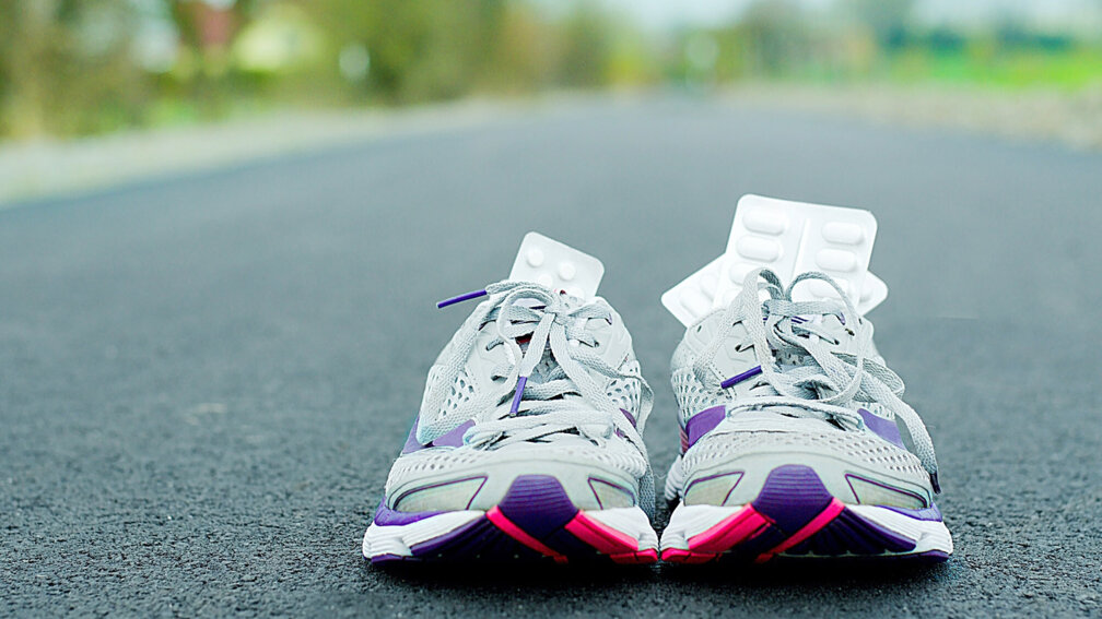 Auf Asphalt stehen weiße Turnschuhe mit Tablettenblistern