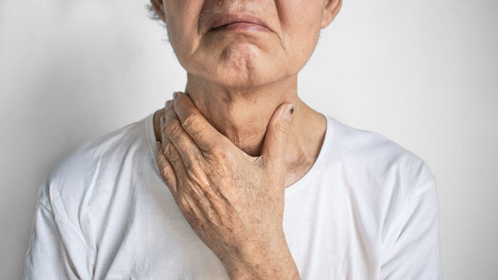 Seniorin hält sich die Hand an die Kehle