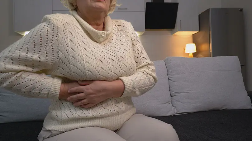 ältere Frau sitzt auf Sofa und greift sich an die rechte Körperseite, direkt über der Leber