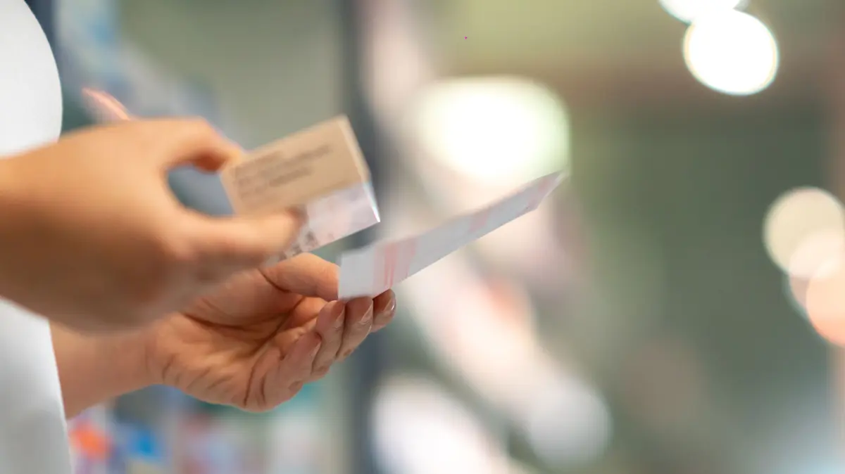 PTahält ein rosa Rezept in der einen Hand und eine Arzneimittelverpackung in der anderen