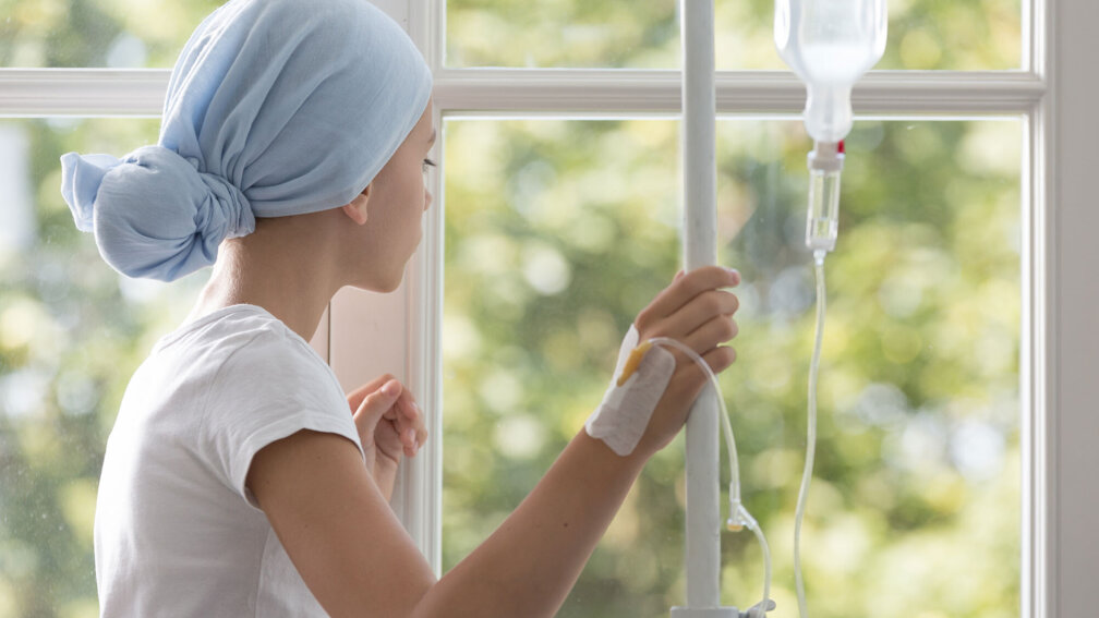 Krebskrankes Kind steht am Fenster mit Infusionsflasche